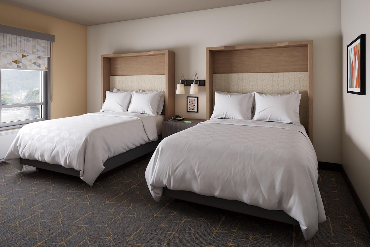 A hotel room with two beds, a window with a view, and a wall-mounted lamp.