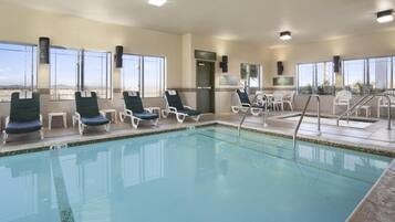 A pool area with lounge chairs, a lifeguard chair, and a sign indicating an emergency exit.