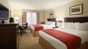 A hotel room with two beds, a desk with a TV, a chair, and a window with curtains.