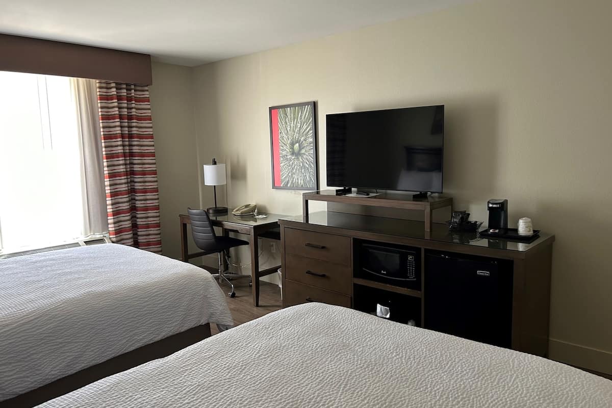 A hotel room with two beds, a desk with a computer, a flat-screen TV, a coffee maker, and a microwave.