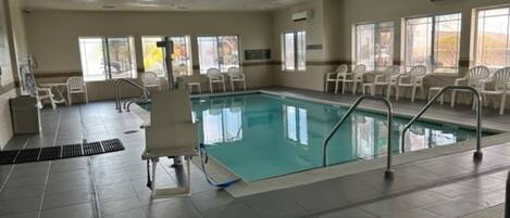 Une grande piscine intérieure à l’eau d’un bleu limpide, entourée de chaises blanches et d’un poste de surveillance pour les sauveteurs.