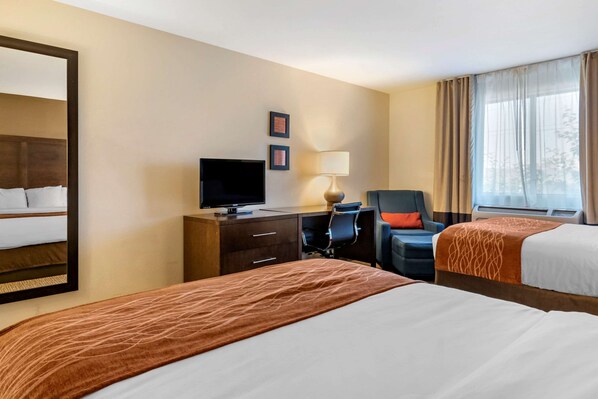 A hotel room with two beds, a desk with a computer, a chair, a TV, and a window with curtains.