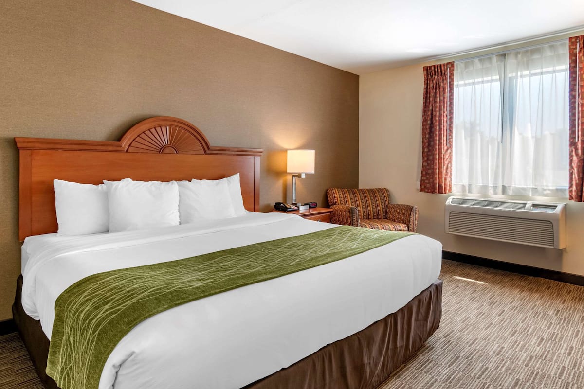 Una habitación de hotel con una cama grande, una silla, una lámpara y un equipo de aire acondicionado.