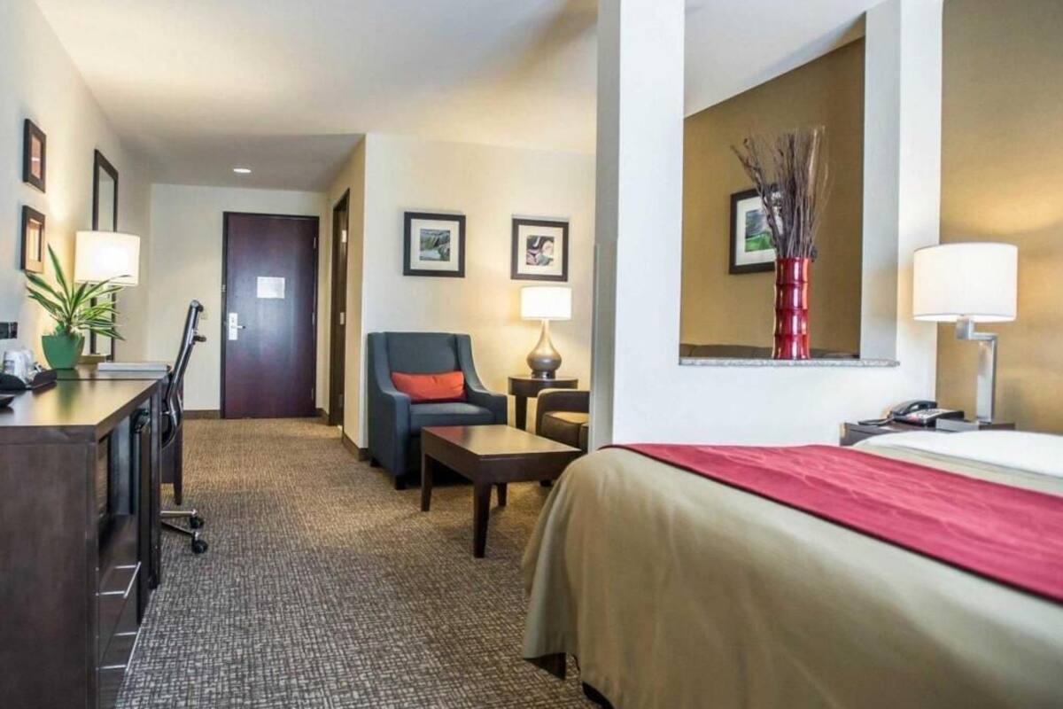 Habitación de hotel con cama, escritorio, silla, lámpara y una pequeña mesa.