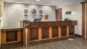 A reception area with a stone wall, a sign for Comfort Inn, a counter with a coffee machine, and a wooden cabinet.