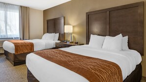 A hotel room with two beds, a nightstand with a lamp, and a window with curtains.