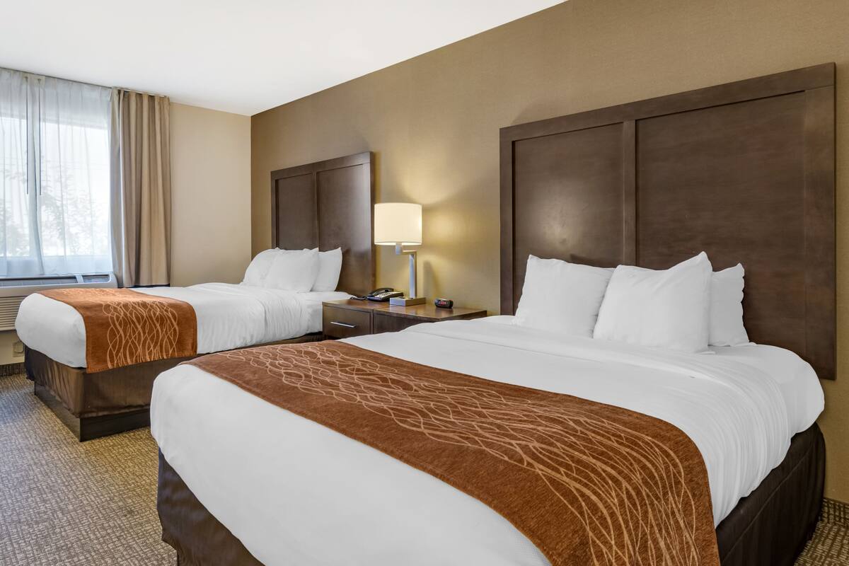 Una habitación de hotel con dos camas, una mesita de noche con lámpara y una ventana con cortinas.