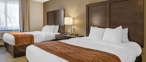 Una habitación de hotel con dos camas, una mesita de noche con lámpara y una ventana con cortinas.