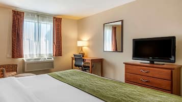 A hotel room with a bed, a desk with a chair, a television, and a window with curtains.