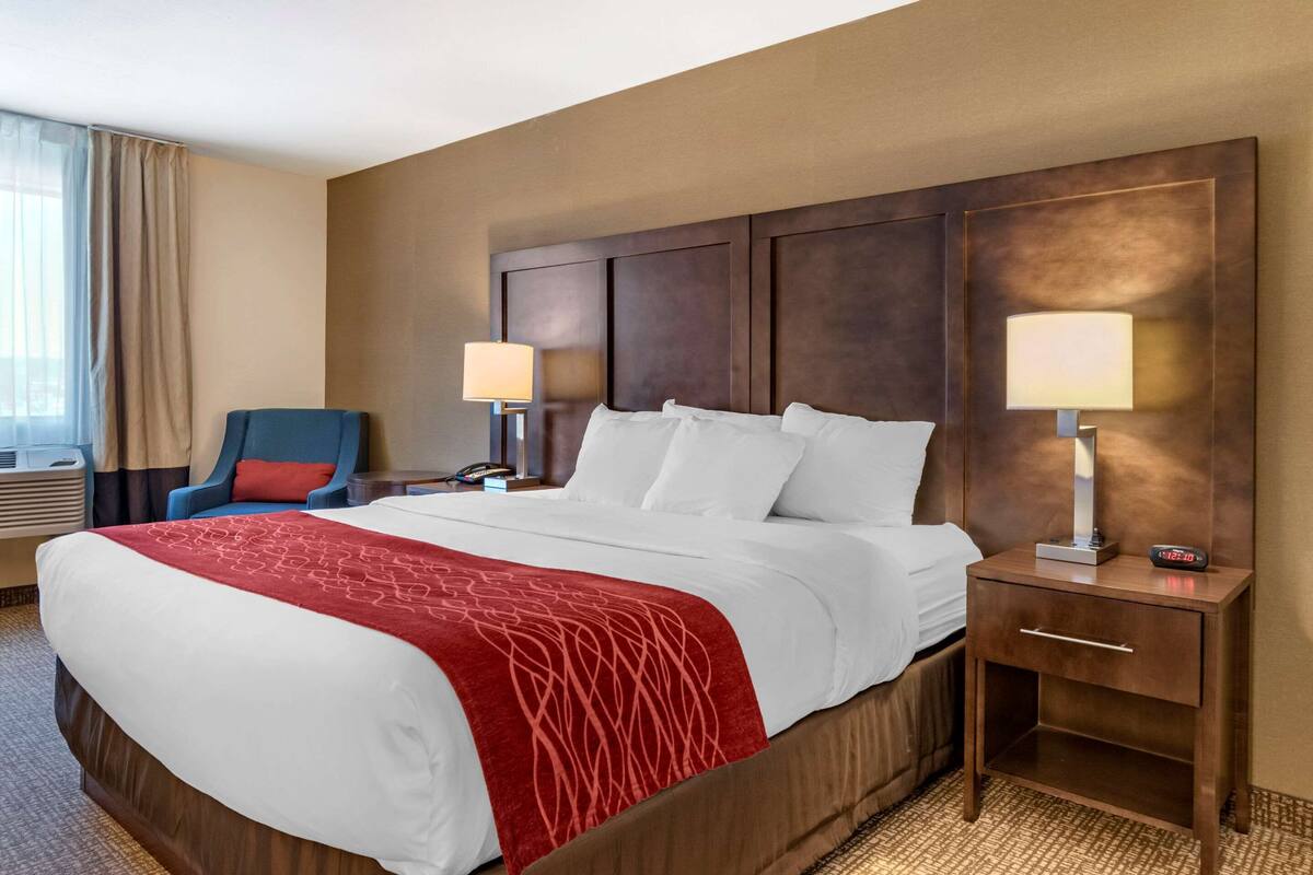 Una habitación de hotel con una cama grande, dos mesitas de noche con lámparas, una silla y una ventana con cortinas.