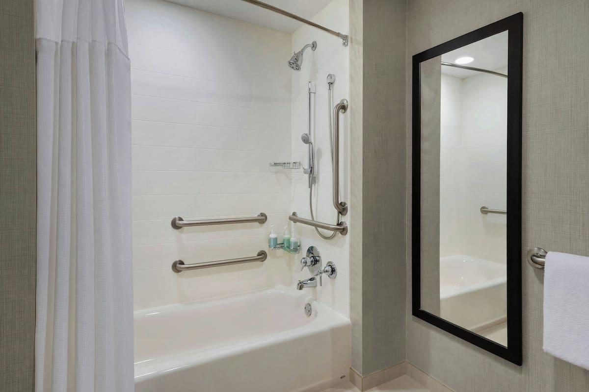 A modern bathroom with a bathtub, shower, and handrails.