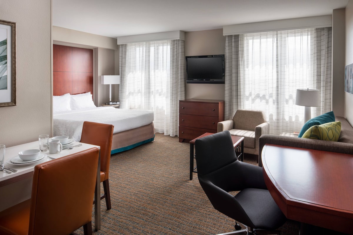 A hotel room with a bed, a desk with chairs, a television, and a dining area.