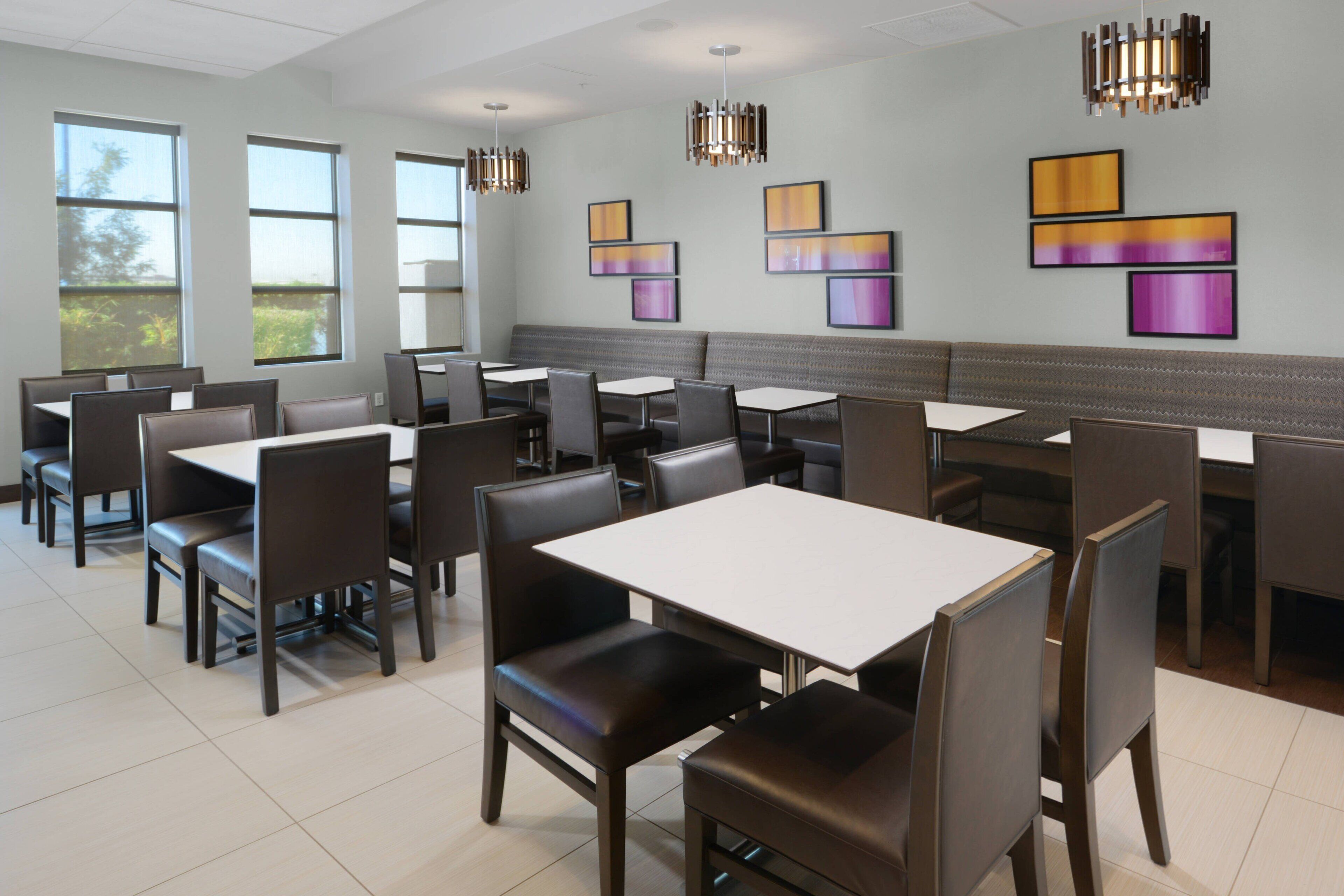 A modern dining area with booths and tables, large windows, and abstract wall art.