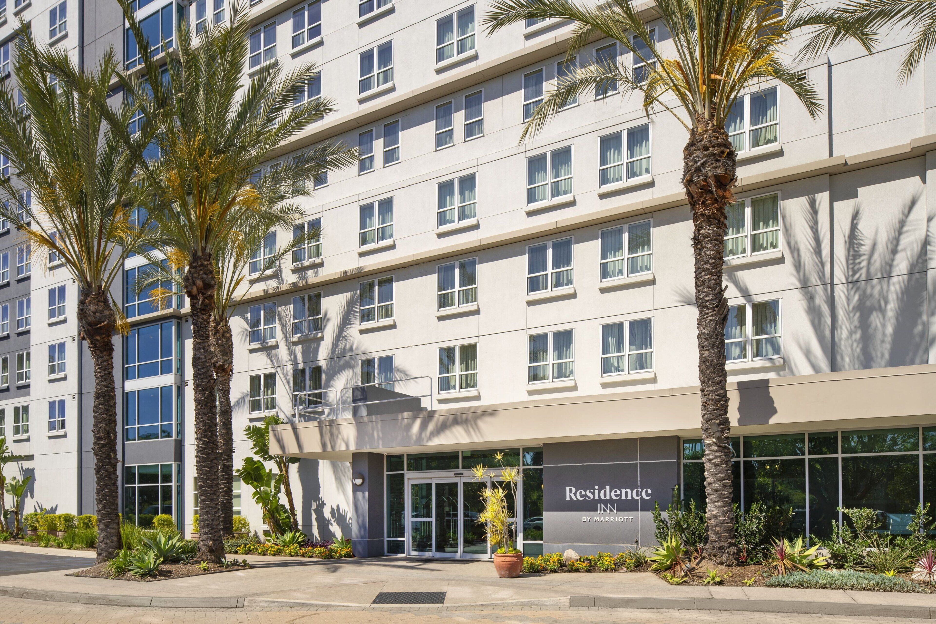 A multi-story hotel with a modern facade, large windows, and palm trees in the foreground.