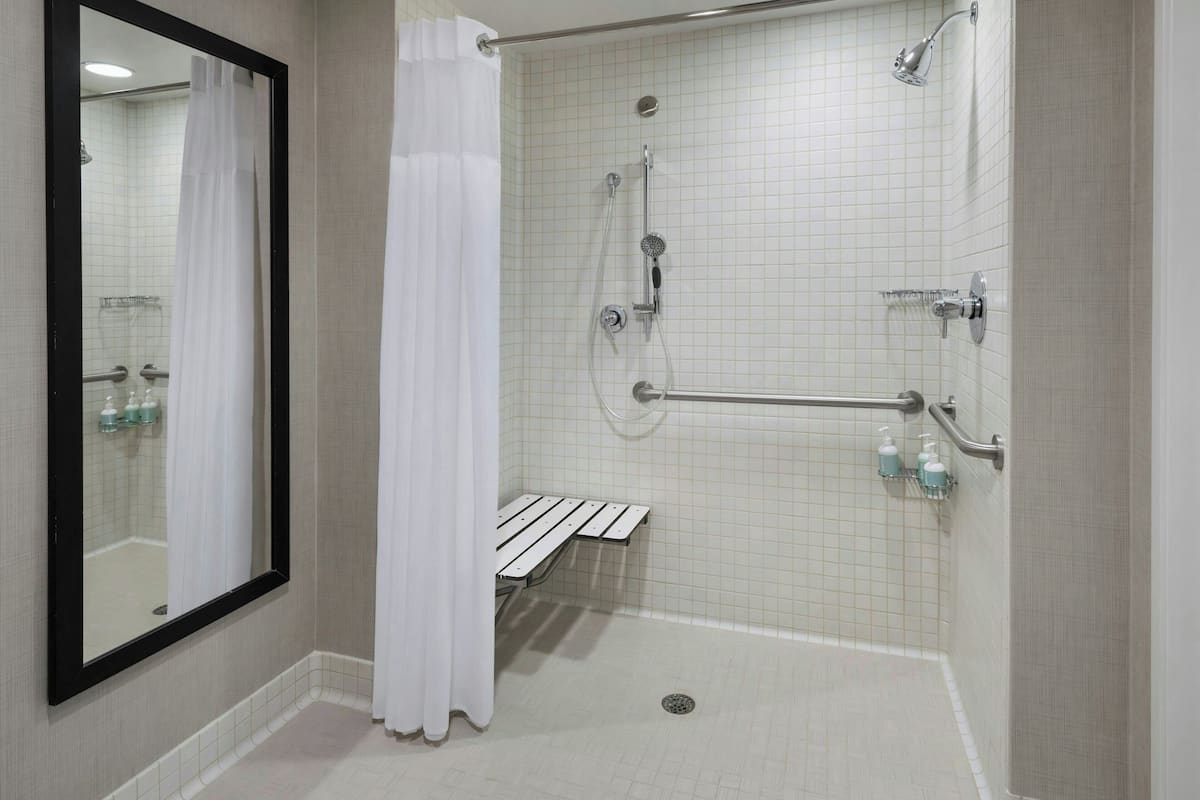 A walk-in shower with a bench, grab bars, and a hand dryer.