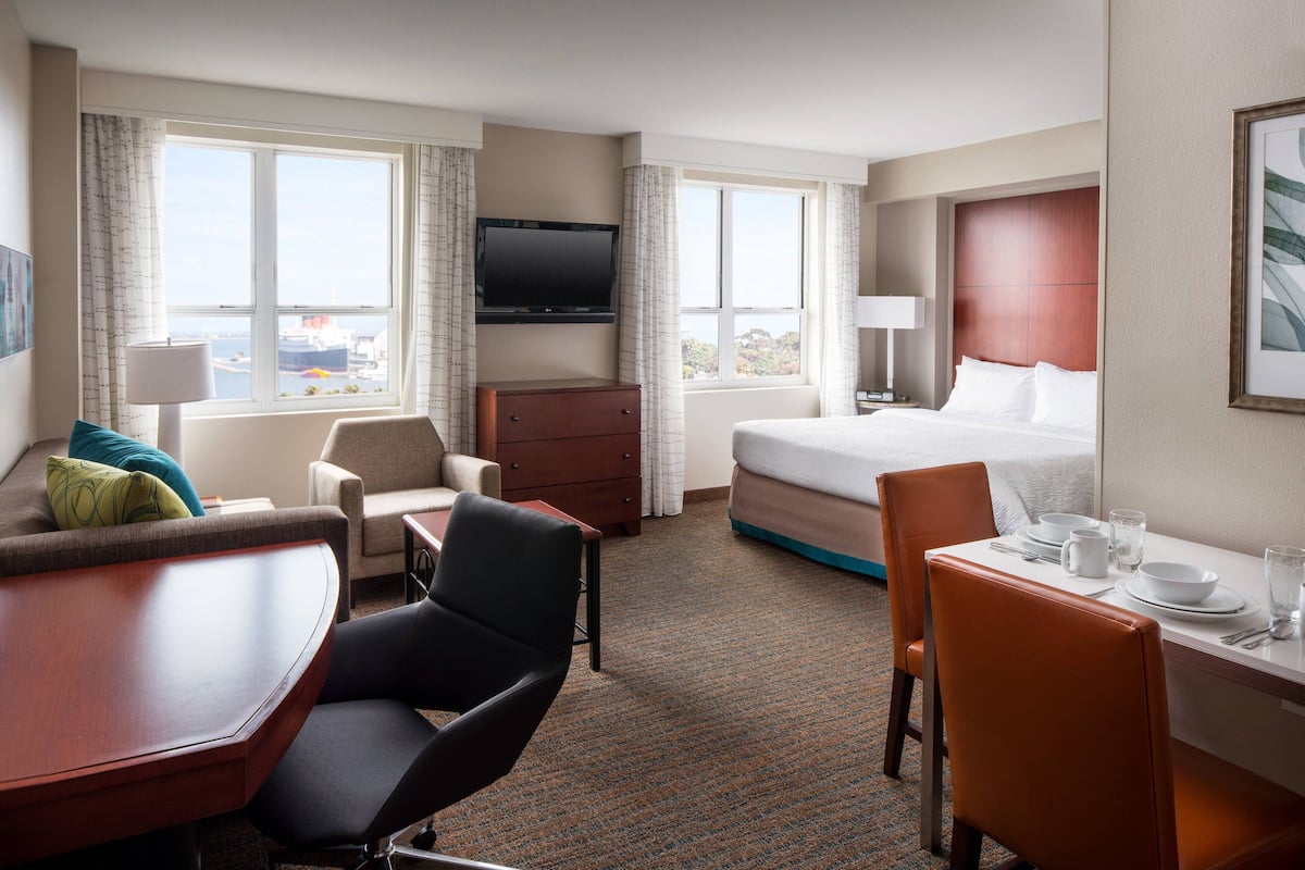 A hotel room with a bed, a desk with a chair, a sofa, a TV, and a window with curtains.