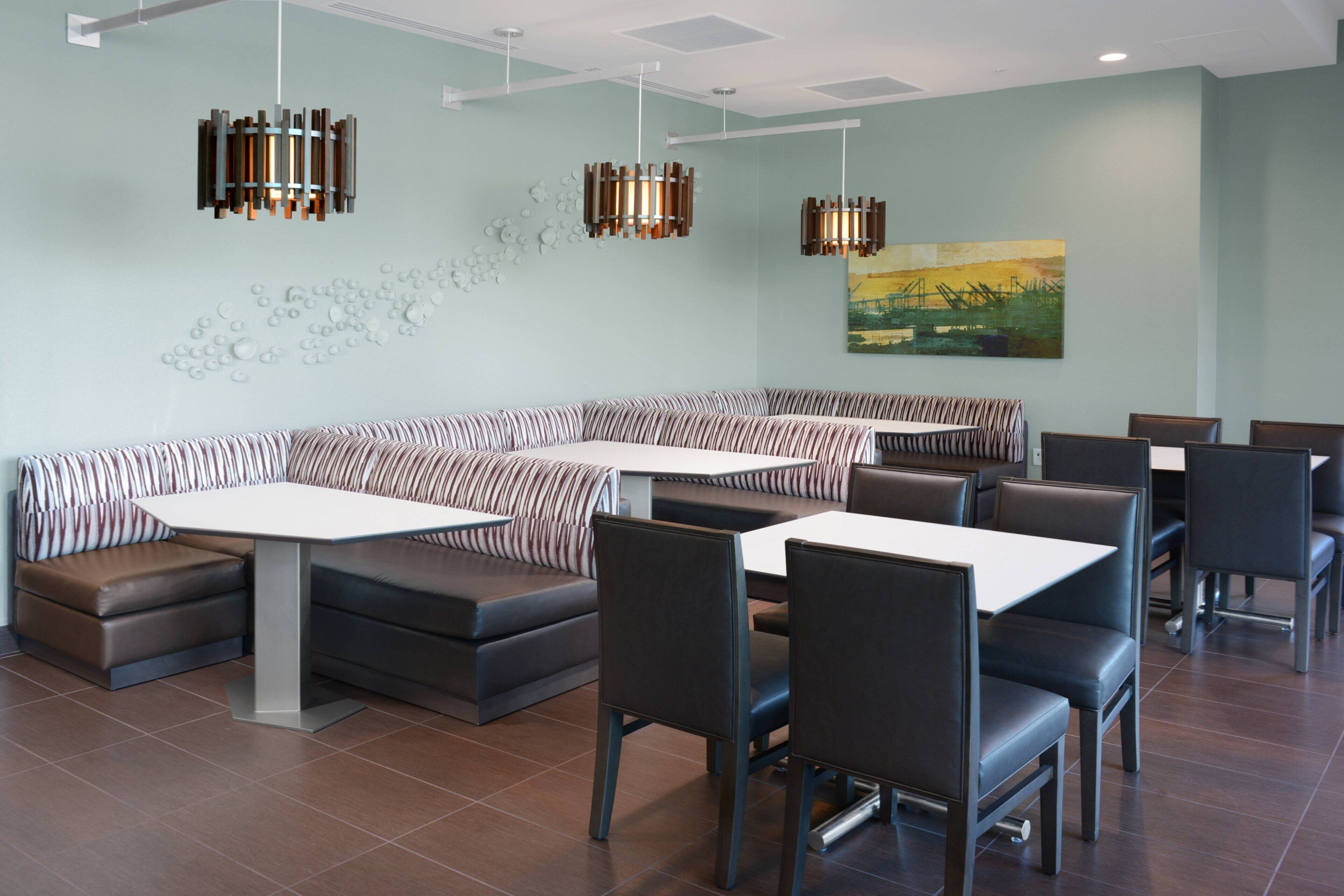 Een modern restaurant met zitbankjes, rechthoekige tafels en hanglampen.