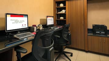 Hotelkamer met een bureau, twee monitoren, een toetsenbord, twee bureaustoelen, een boekenkast en een printer.