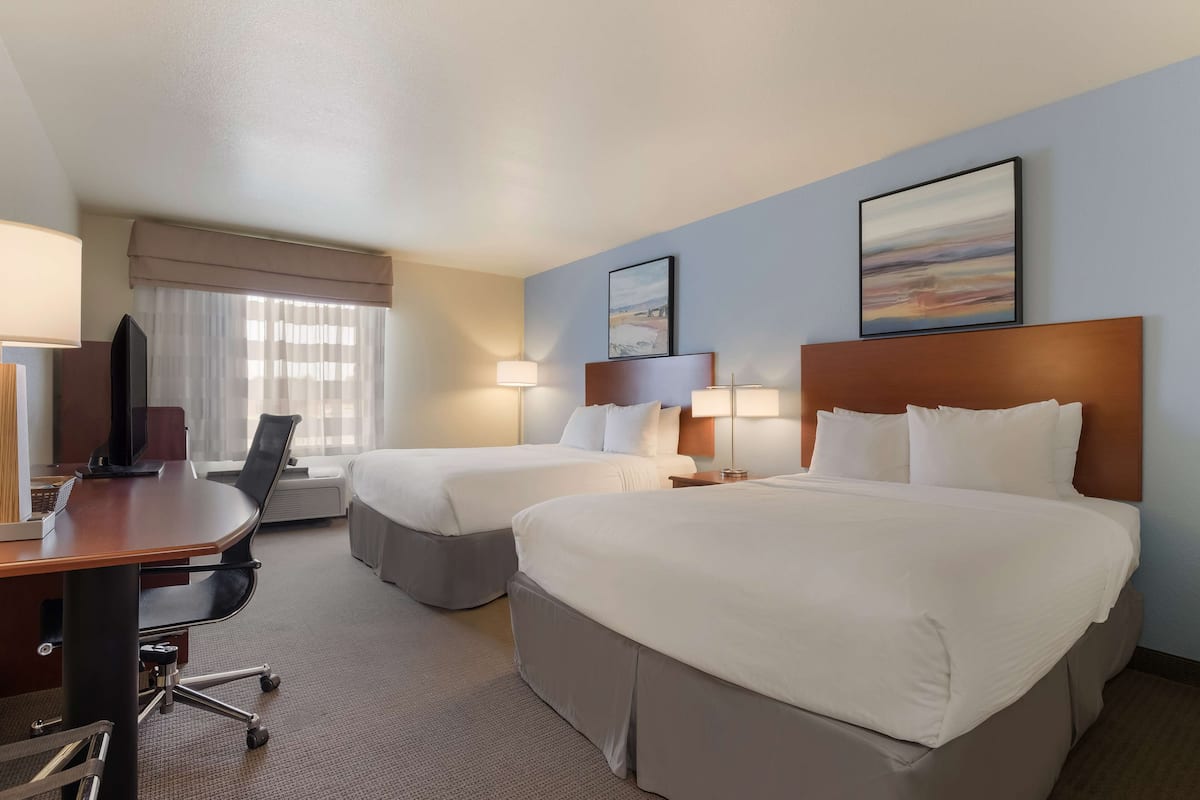 Une chambre d’hôtel avec deux lits, un bureau avec un ordinateur, une chaise et deux lampes.