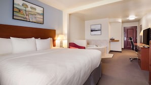 A hotel room with a large bed, a desk, a chair, a TV, and artwork on the walls. - Best Western Coffeyville Central Business District Inn and Suites (Coffeyville)