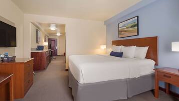 A hotel room with a large bed, a desk, a chair, a TV, and a painting on the wall.