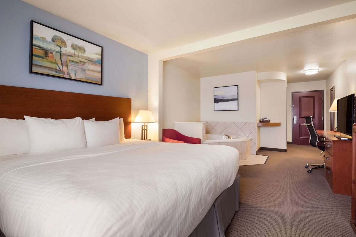 Une chambre d’hôtel avec un grand lit, un bureau avec une chaise, une télévision, une salle de bain avec une baignoire et des œuvres d’art aux murs.