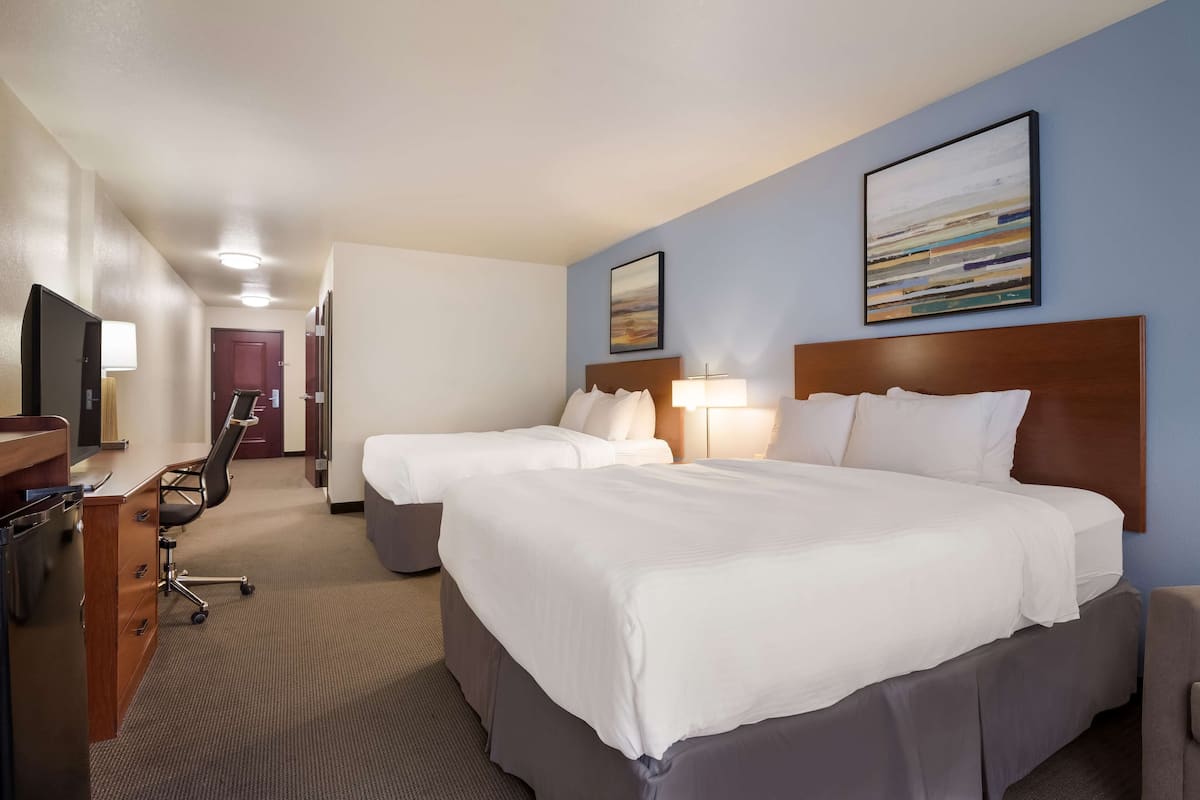 Une chambre d’hôtel avec deux lits, un bureau, une chaise et un téléviseur.