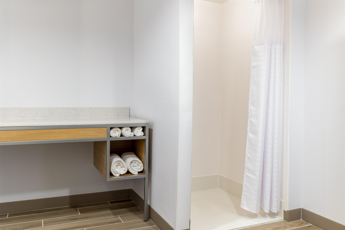 A bathroom with a shower, a towel rack with towels, and a wooden shelf.