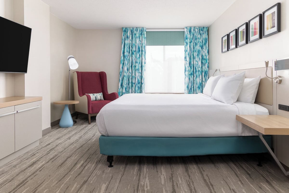 A hotel room with a bed, a chair, a desk, a television, and a window with curtains.