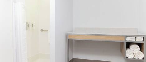 A bathroom with a shower, a towel rack, and a shelf with towels.