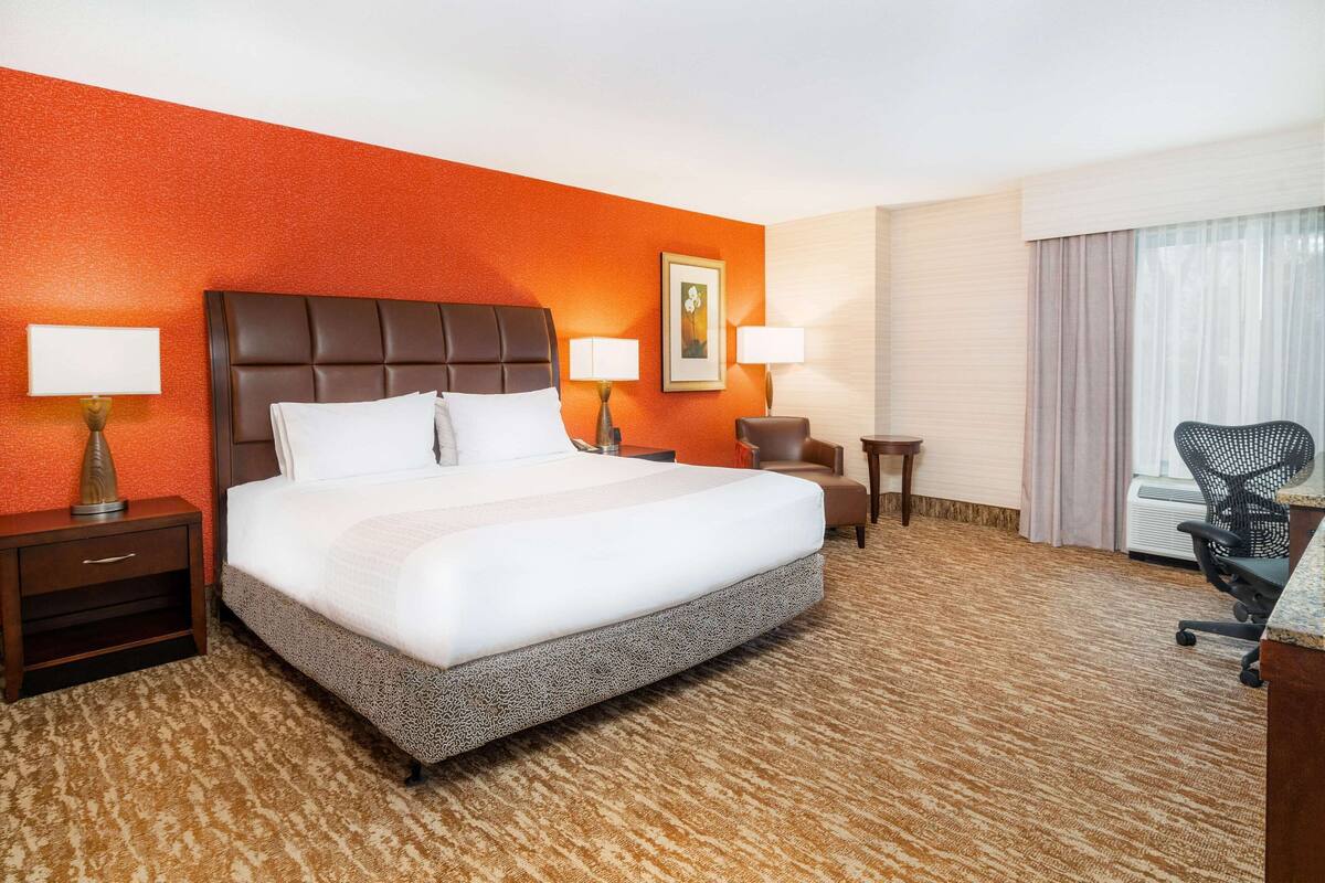 A hotel room with a large bed, two bedside tables with lamps, a chair, and a desk.