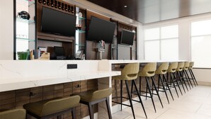 A modern bar area with a long counter, multiple screens, and bar stools. - Hilton Garden Inn Hanover Arundel Mills,  MD (Hanover)