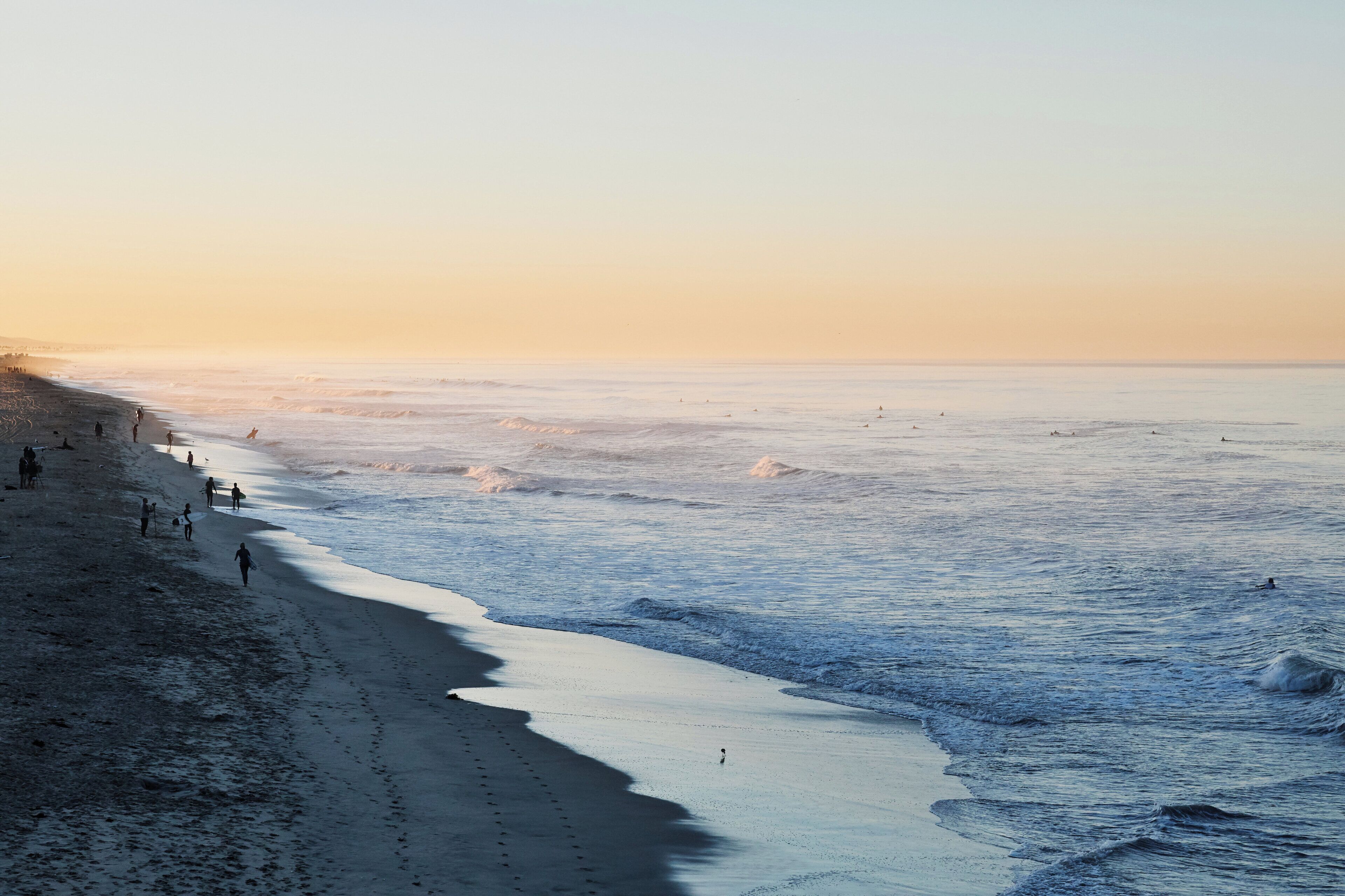 A beach with people walking and surfing, and a clear sky.