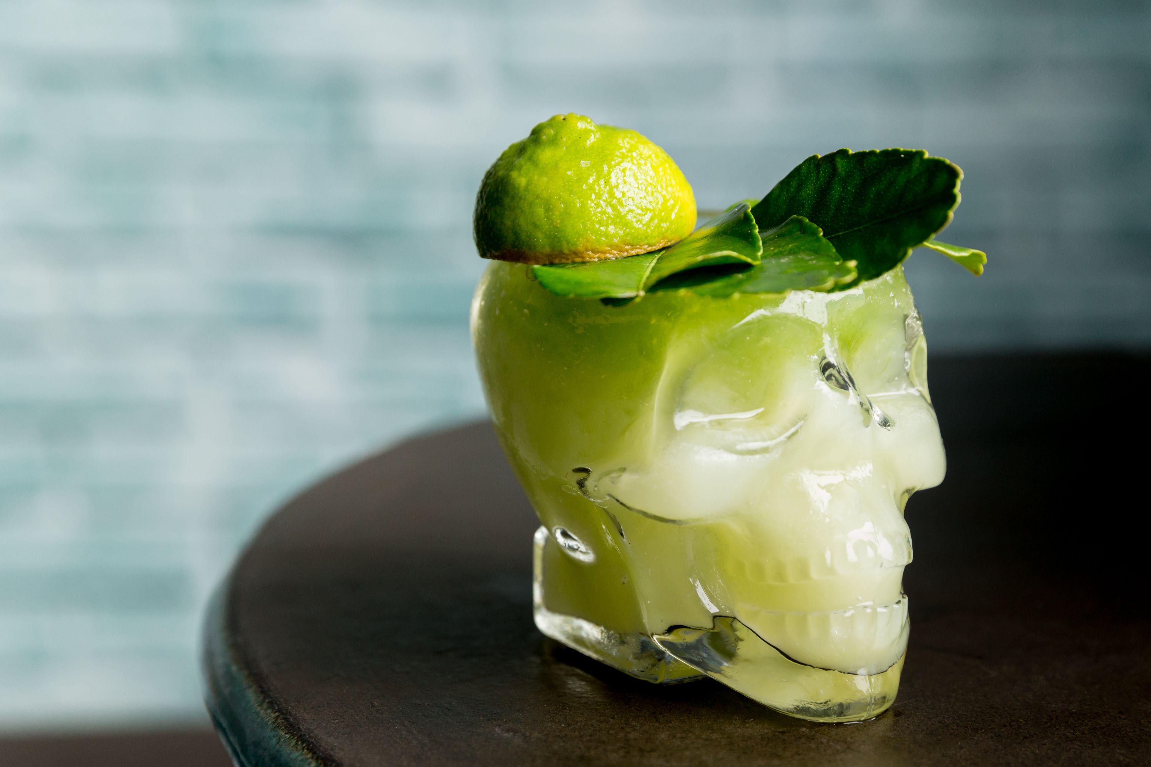 A cocktail in a skull-shaped glass with a lime and mint garnish.