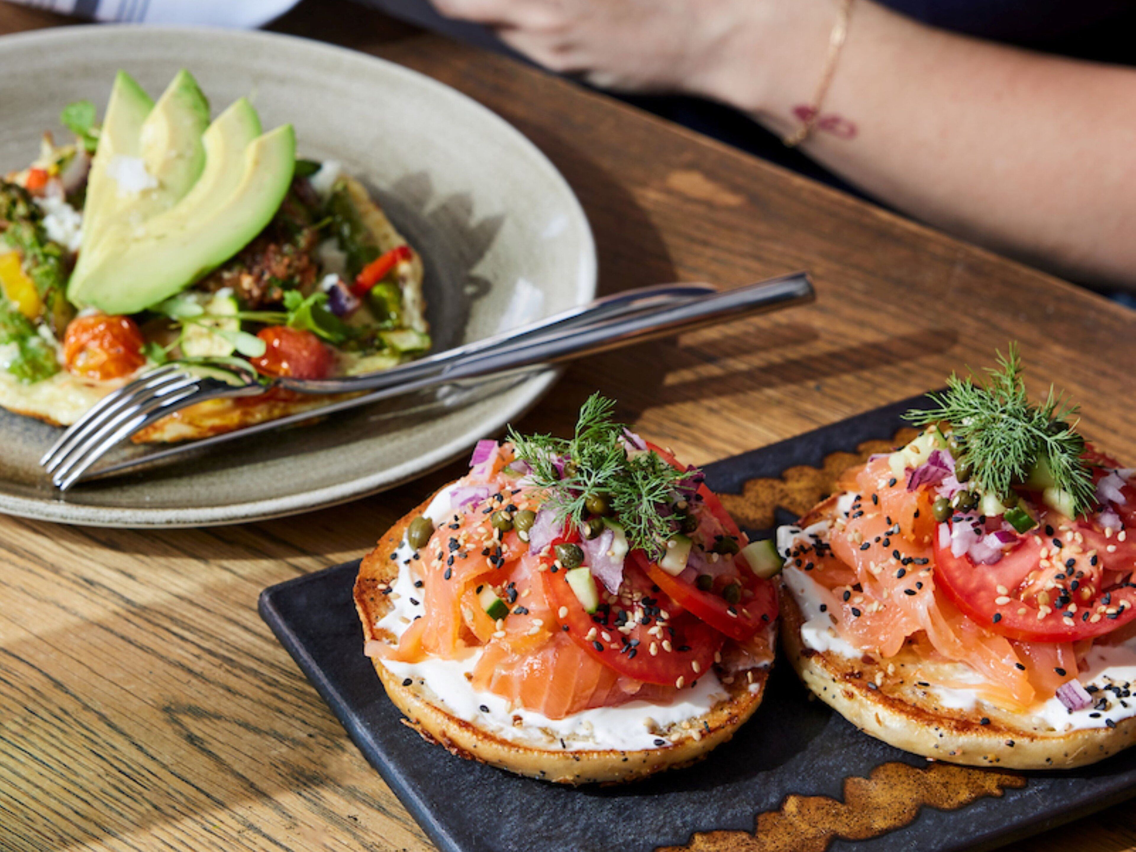 Two open-faced sandwiches on a slate plate, one with avocado and the other with tomatoes and onions.