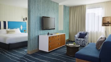 A hotel room with a bed, a sofa, a TV, a side table, and a chair.