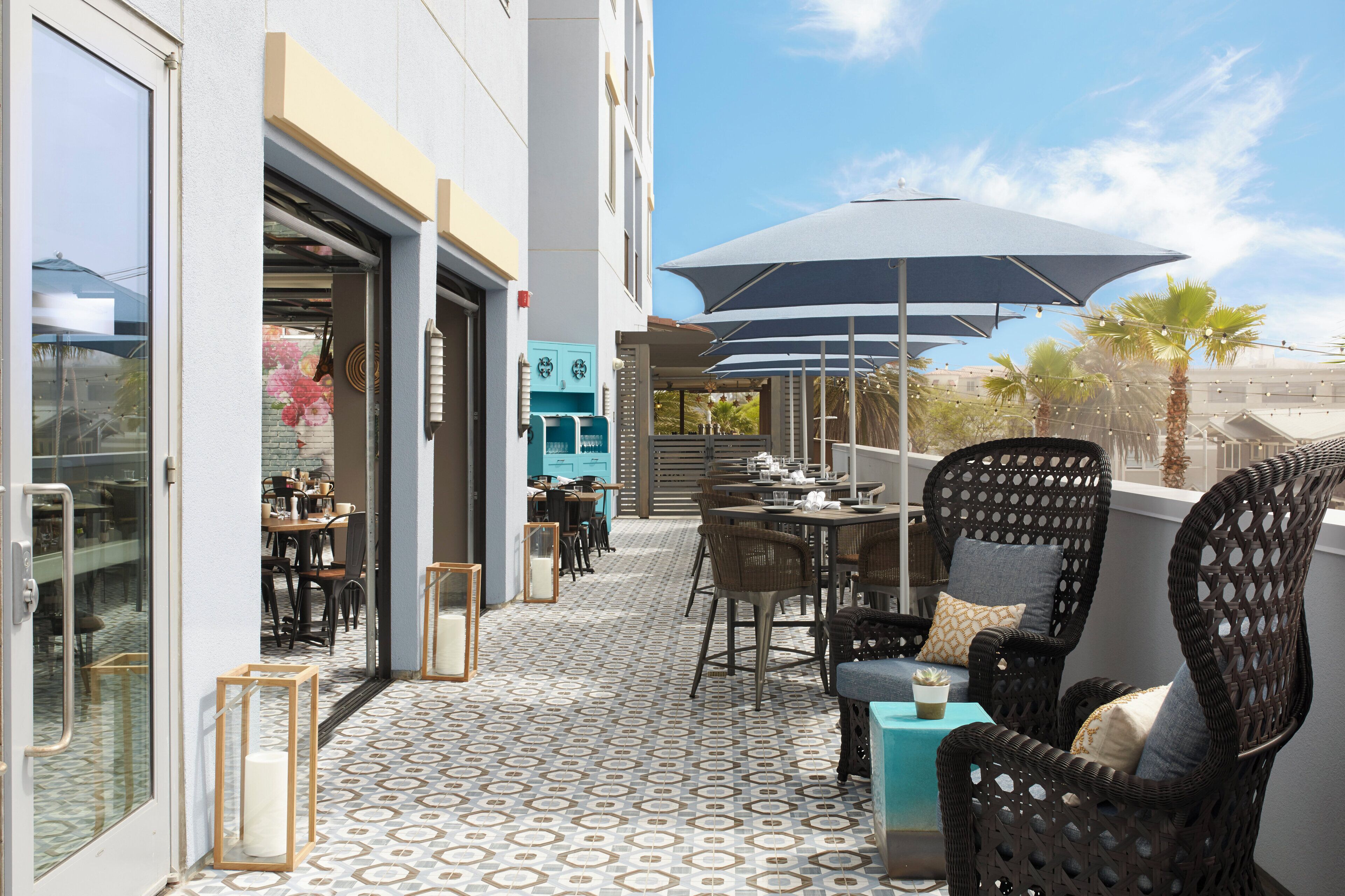 An outdoor seating area with wicker furniture and umbrellas, a patterned floor, and a view of the street.