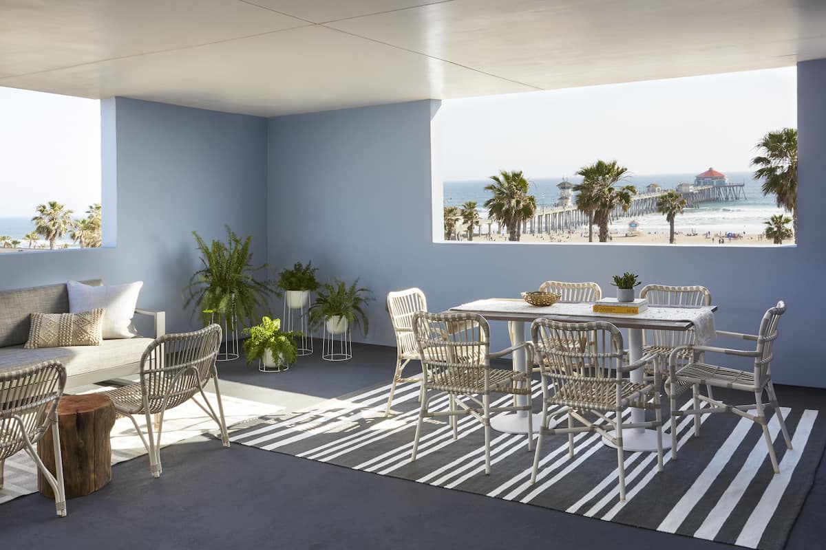 A modern outdoor seating area with a view of the beach and pier, featuring wicker furniture and potted plants.