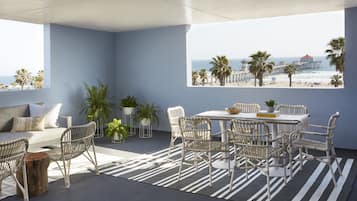 A modern outdoor seating area with a view of the beach and pier, featuring wicker furniture and potted plants.
