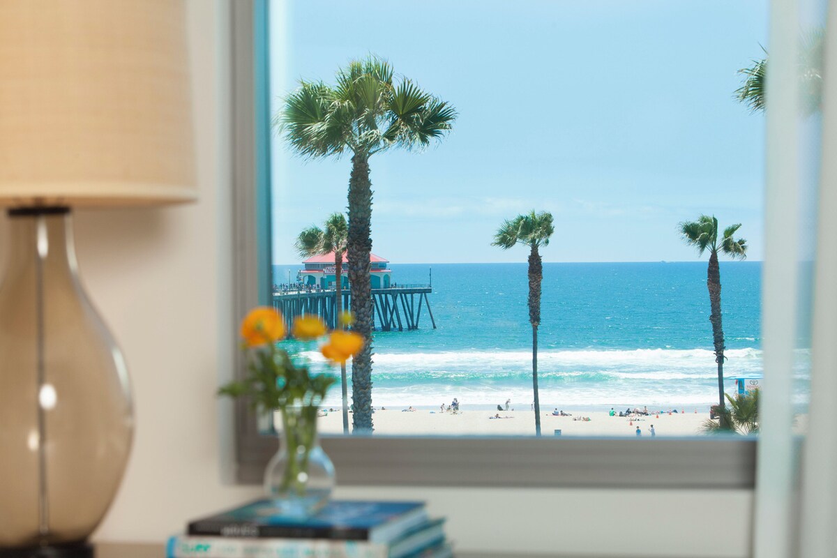 A view of a beach with palm trees, a pier, and the ocean.