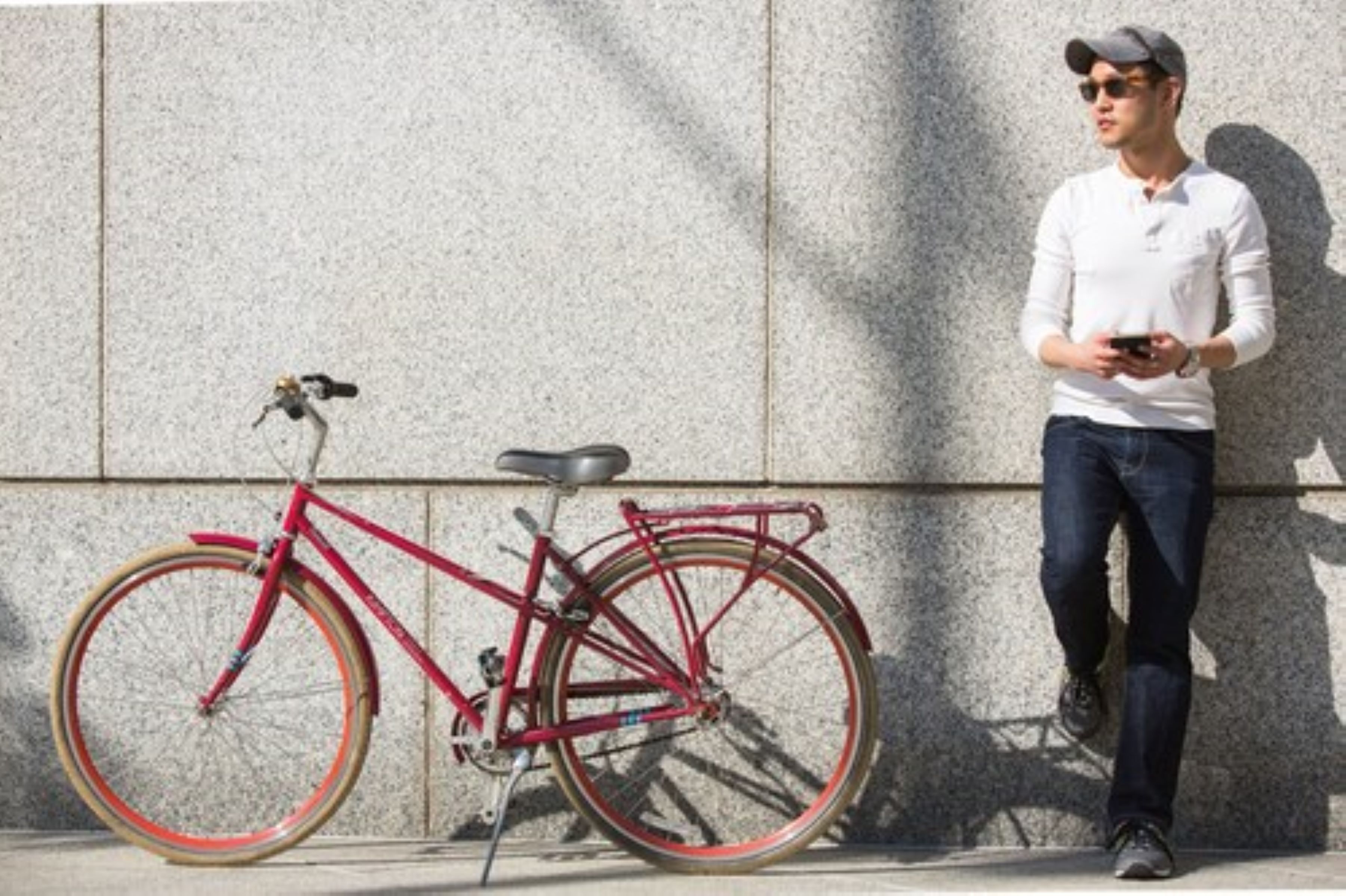 Un vélo rouge est garé contre un mur à la texture particulière.