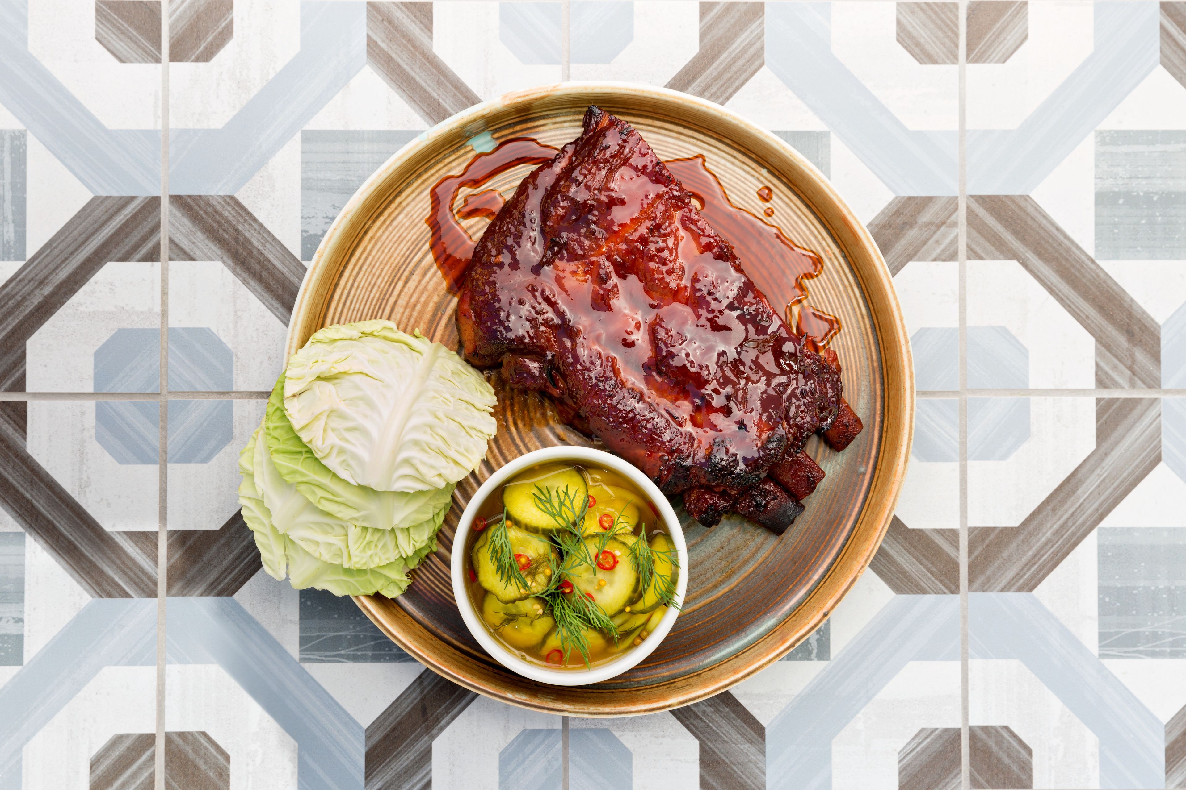 A plate with a glazed meat dish, a side of pickled vegetables, and a cabbage.