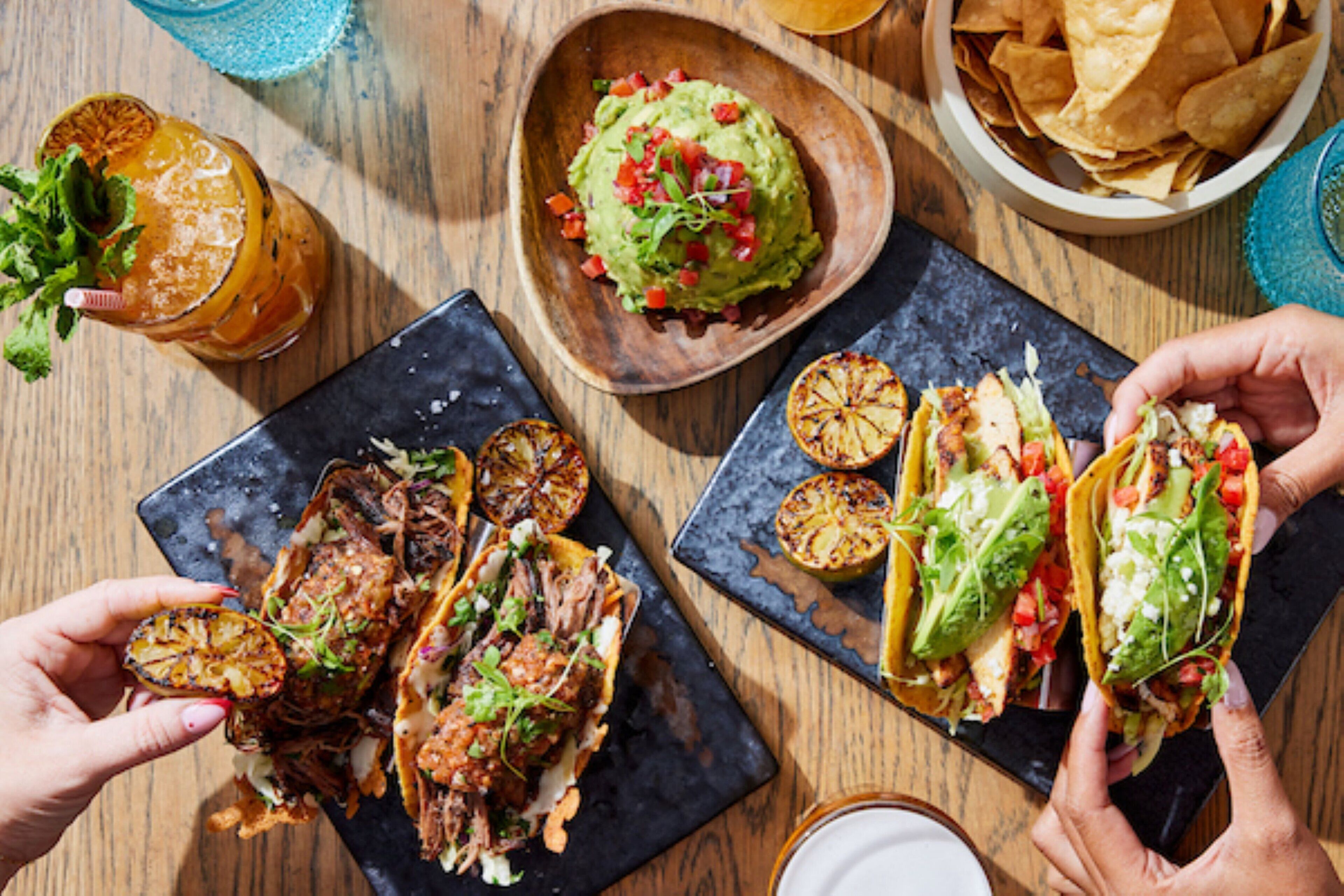A table with various dishes, including tacos, guacamole, and grilled vegetables.