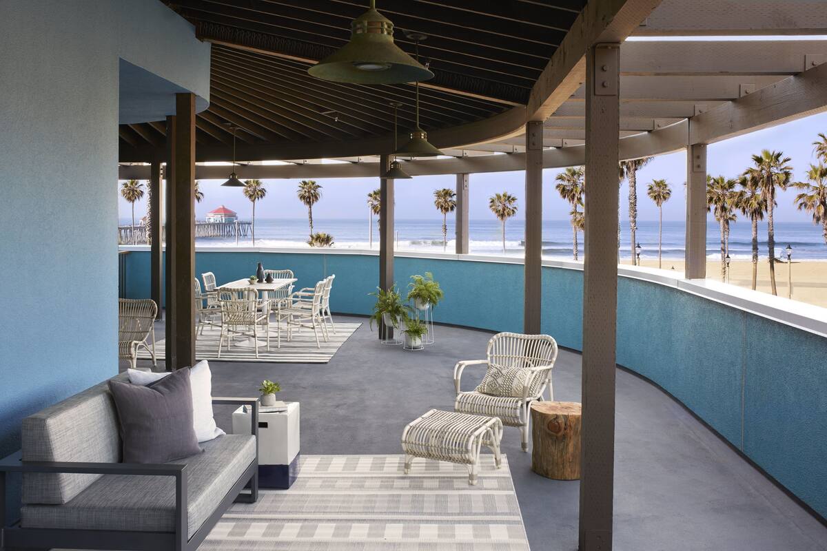 A covered outdoor seating area with a view of the beach, featuring a sofa, chairs, and a dining table.