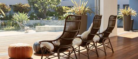 A modern outdoor seating area with wicker chairs and a round ottoman, overlooking a landscaped garden and a building with balconies.