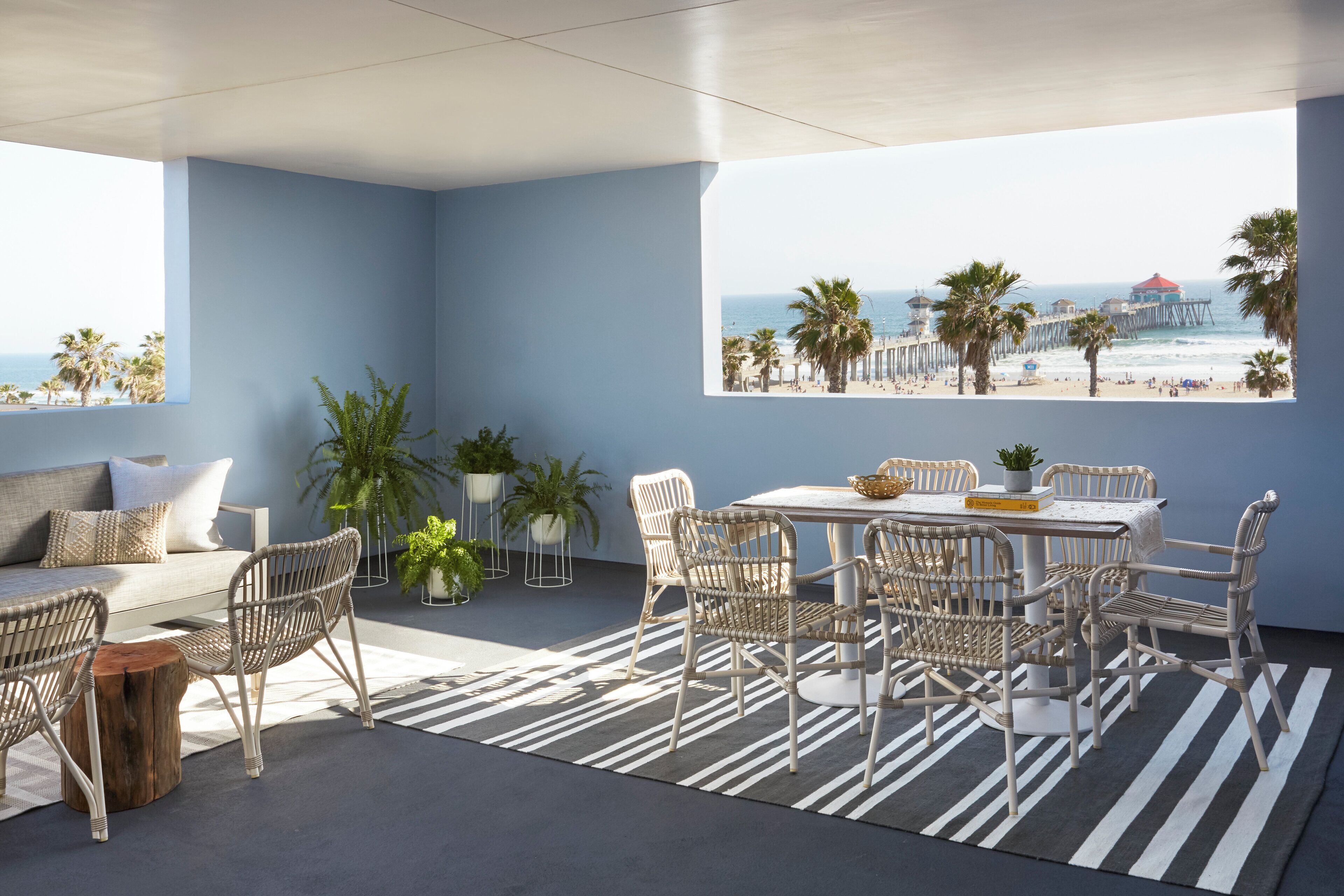 A modern interior with a view of the beach, featuring a sofa, chairs, a table, and potted plants.
