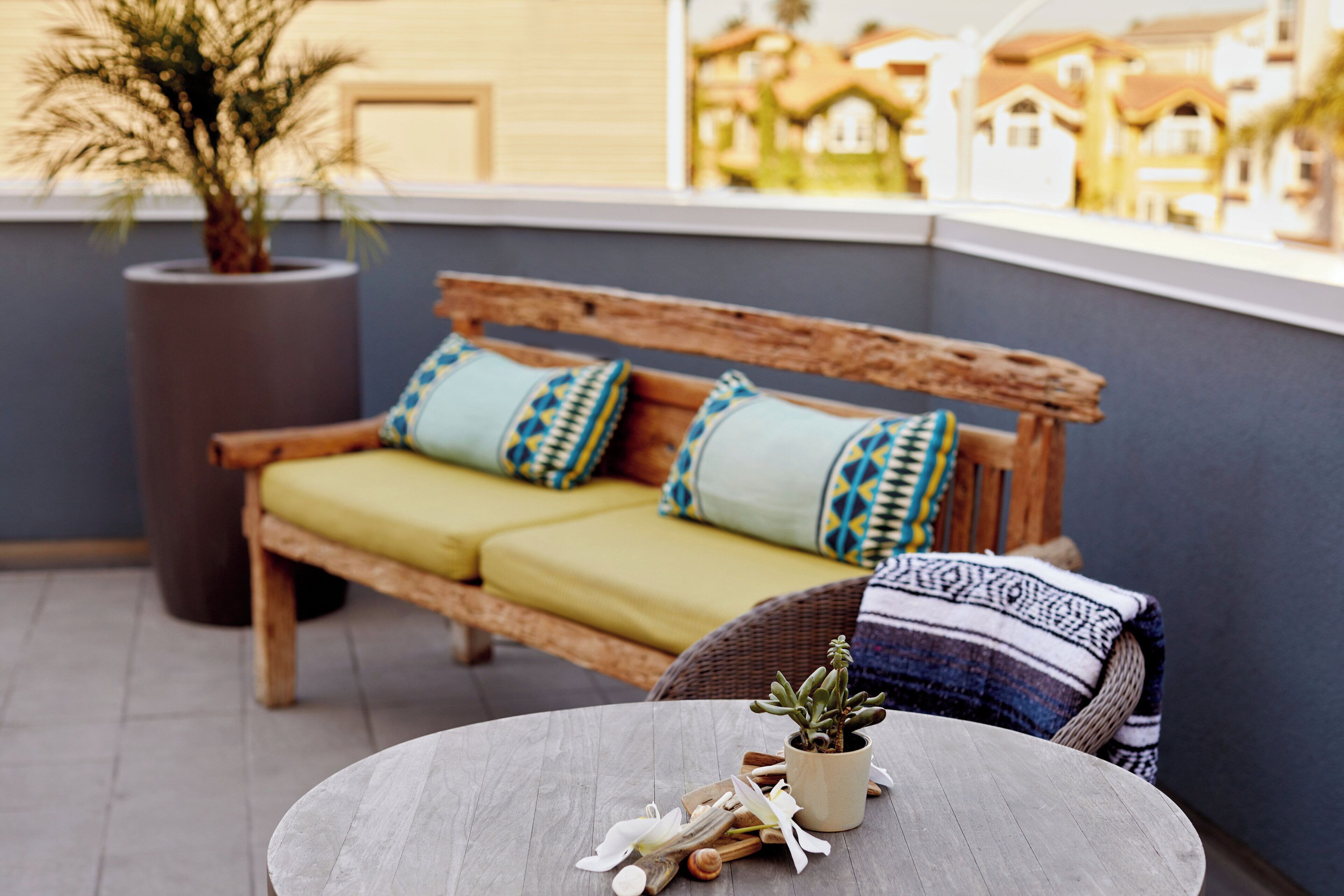A wooden bench with cushions and a potted plant on a balcony.