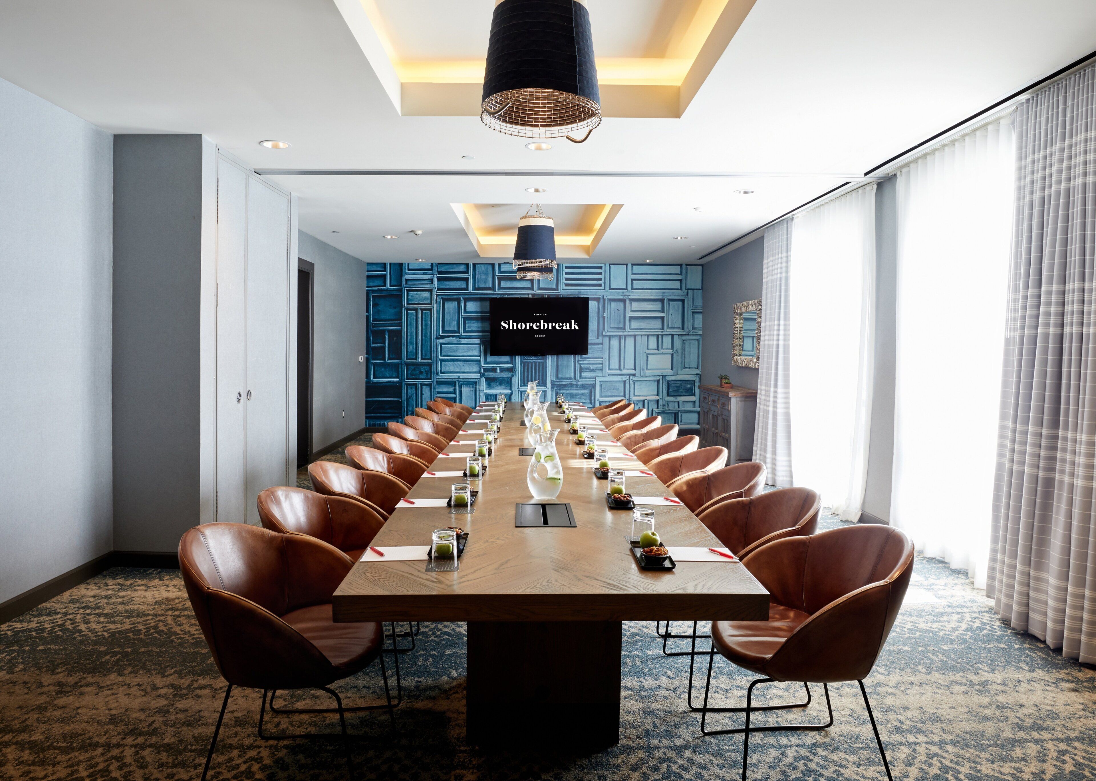 A conference room with a long table, leather chairs, and a television screen displaying 'Shorebreak.'