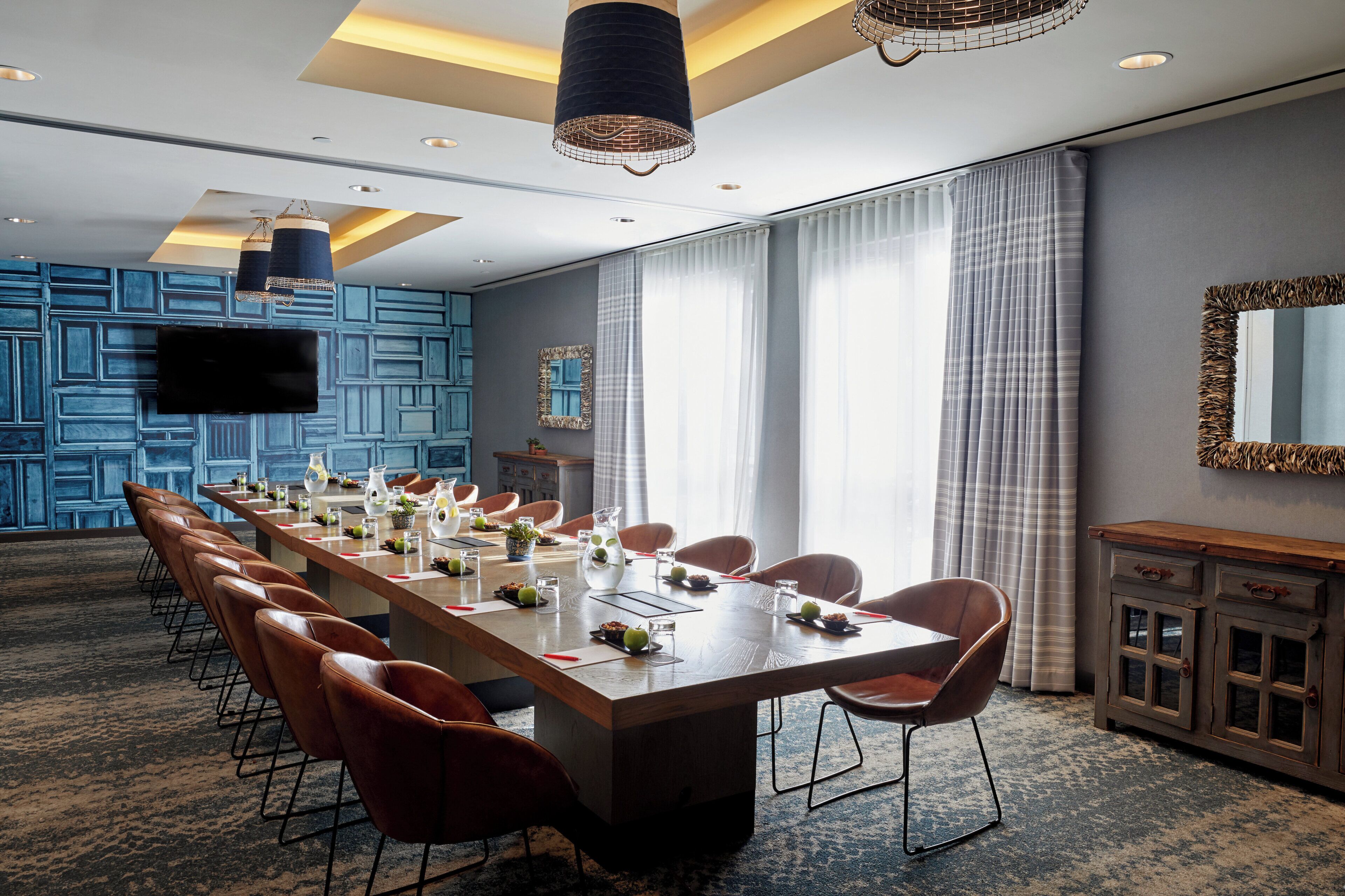 A conference room with a long table, chairs, a TV, and a patterned wall.