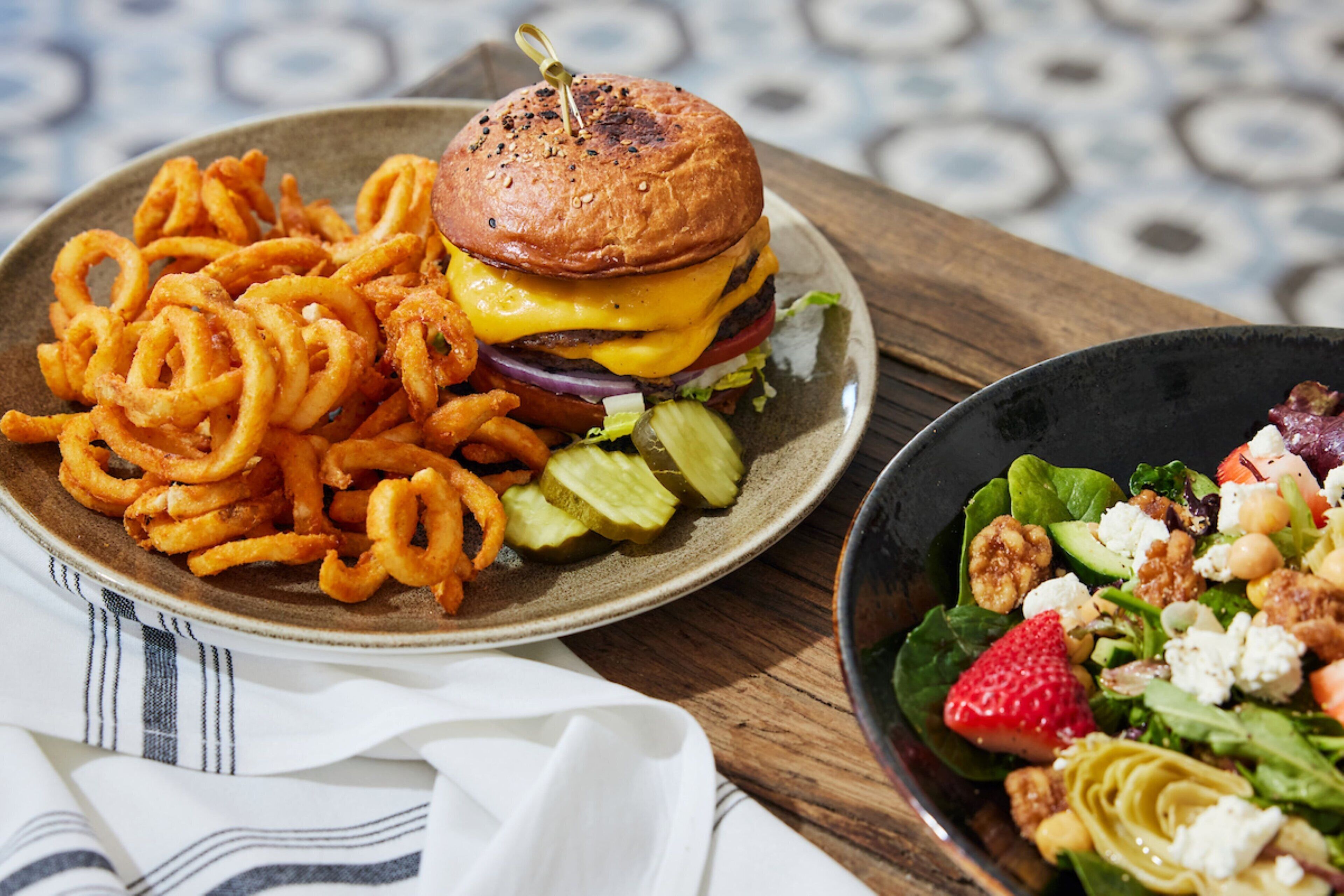 A plate of onion rings, a burger, and a salad with strawberries and nuts.